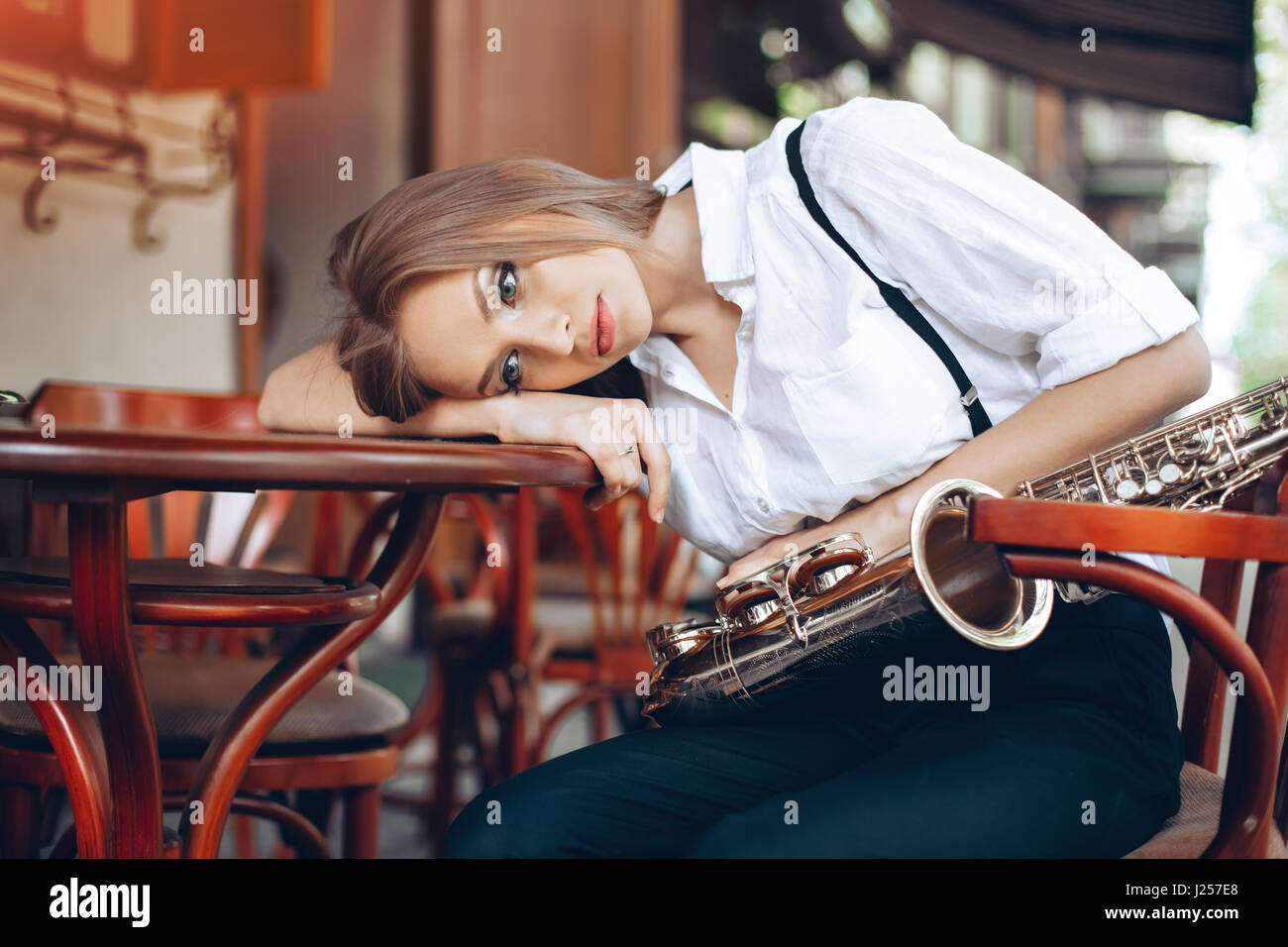 Jeune fille attirante en chemise blanche avec un saxophone assis près de caffe shop - Piscine dans sity. Sexy young woman looking at camera avec sax. Banque D'Images