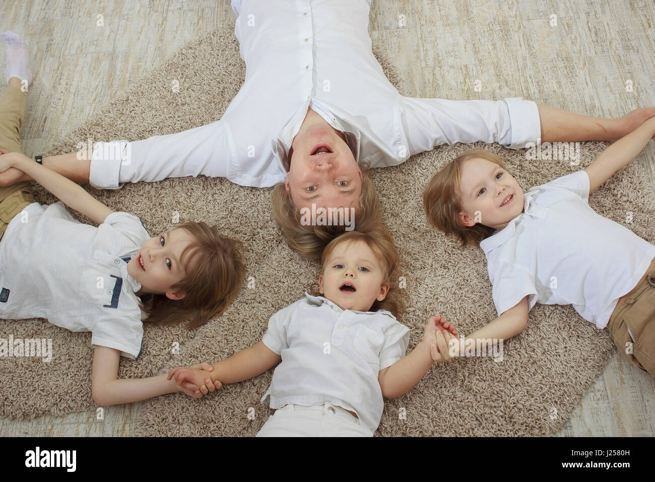 Vue de dessus du jeune père de trois adorables petits fils lying on floor Banque D'Images