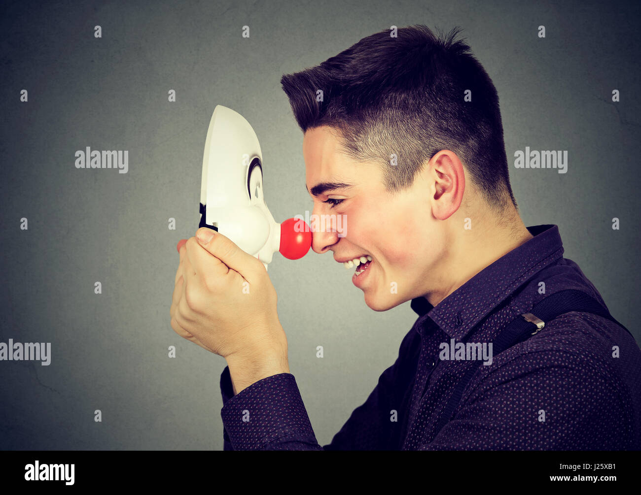 Laughing Man avec masque de clown sur fond de mur gris Banque D'Images