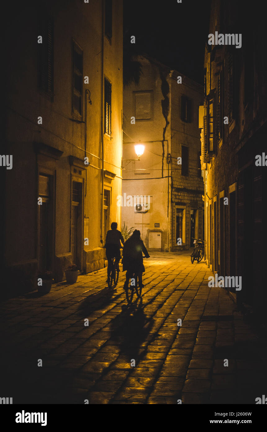 Silhouette de deux personnes la bicyclette vers le bas de la rue Pierre de nuit, Vis, Croatie Banque D'Images