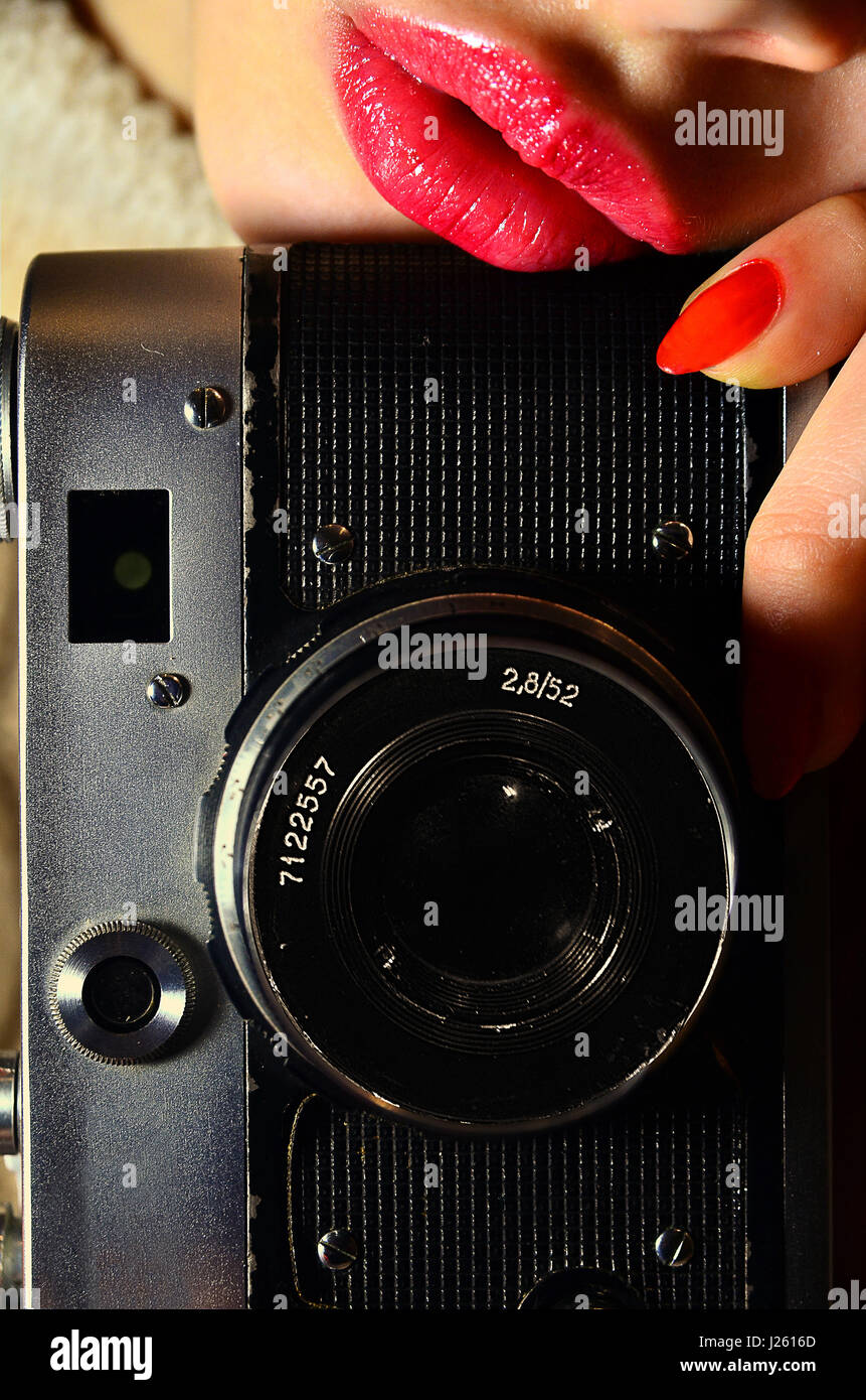 Girl holding l'appareil photo à la main, appuyé contre ses lèvres. Photo couleur. Lèvres roses, red nails, photo verticale Banque D'Images