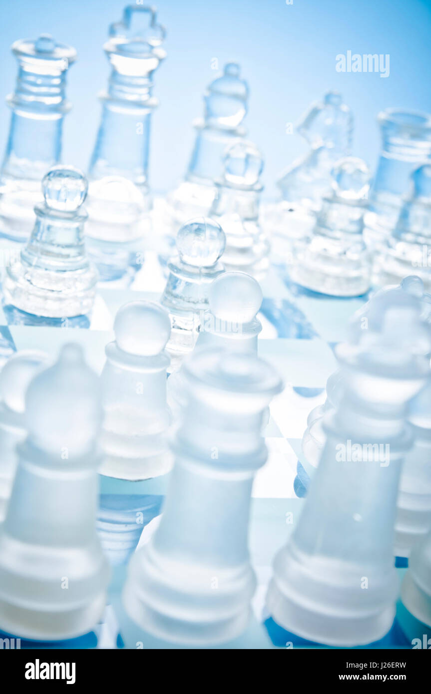 Gros plan de pièces d'échecs en verre mat et transparent sur un échiquier en verre bleu, vu de dessus sous un angle diagonal Banque D'Images