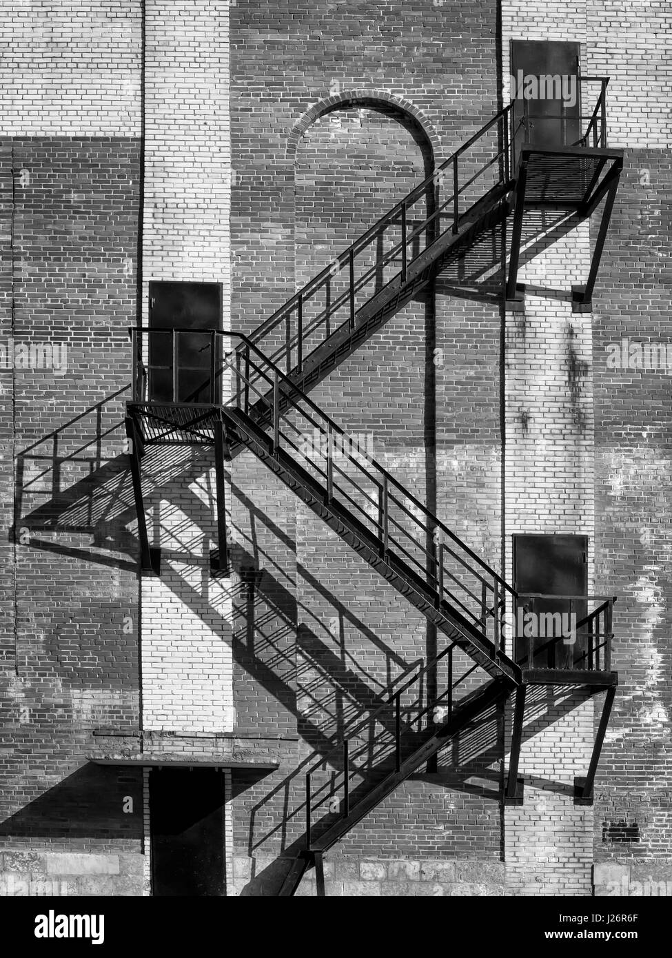 L'escalier en acier et portes noir sur ancien bâtiment industriel mur de briques. Le soleil direct. Photo en noir et blanc Banque D'Images