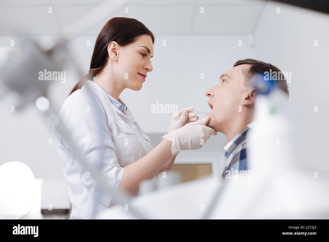 L'examen de la gorge. Smiling woman holding oto-rhino-laryngologiste de toucher l'instrument de son menton tout en le traitant de visiteur Banque D'Images