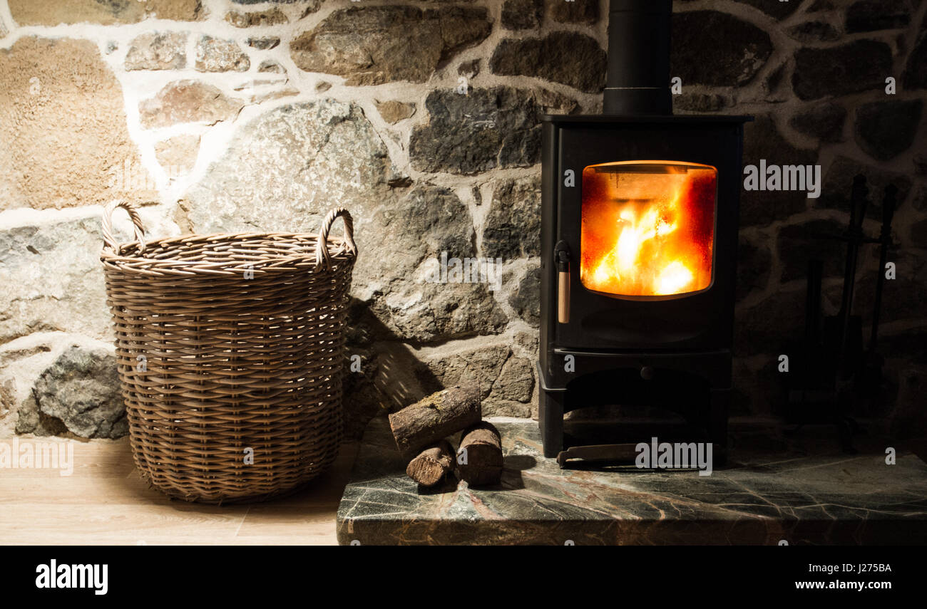 Le Foyer et cheminée dans l'intérieur d'une maison fortifiée en pierre avec un poêle à bois, grumes et panier dans une atmosphère accueillante, chaleureuse scène. Banque D'Images