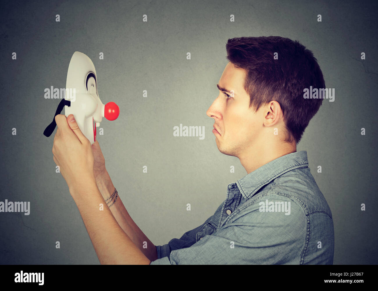 Portrait of a sad man holding à happy clown mask Banque D'Images