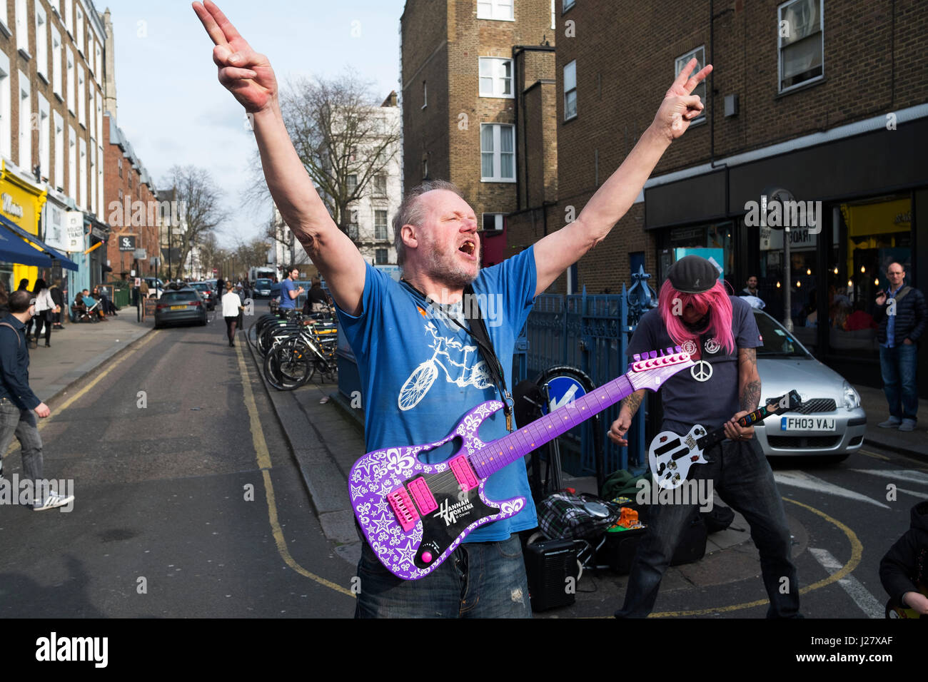 Deux hommes sur Portobello Road effectuer leurs arts de la performance pour  des groupes de la musique tout en faisant semblant de jouer jouets en plastique  guitares dans Londres, Angleterre, Royaume-Uni. L'un