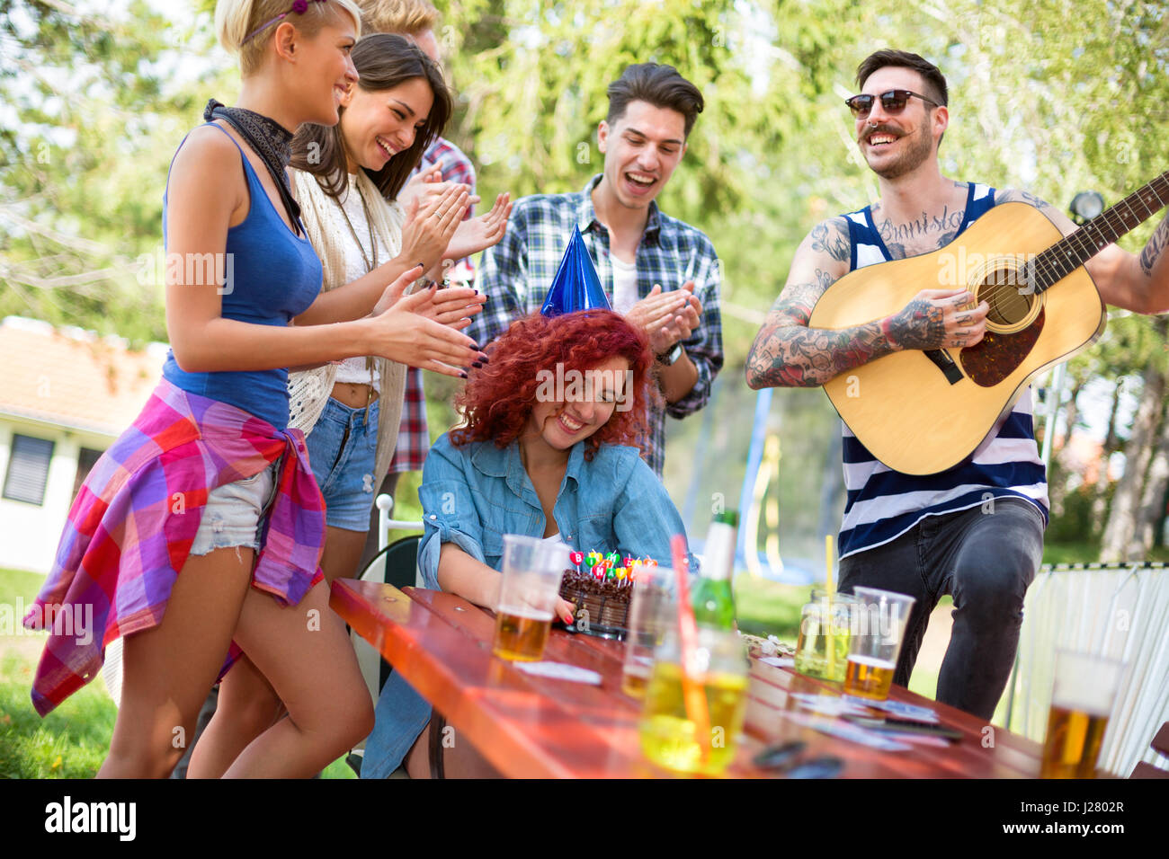 Gâteau d'anniversaire avec des bougies colorées et guy avec guitare font partie de l'anniversaire des filles dans la nature Banque D'Images