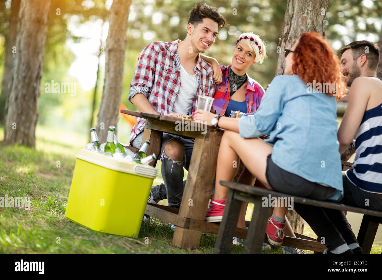 Les filles et les gars s'assoit sur le banc à table en bois dans la forêt, à boire de la bière et faire des plaisanteries Banque D'Images