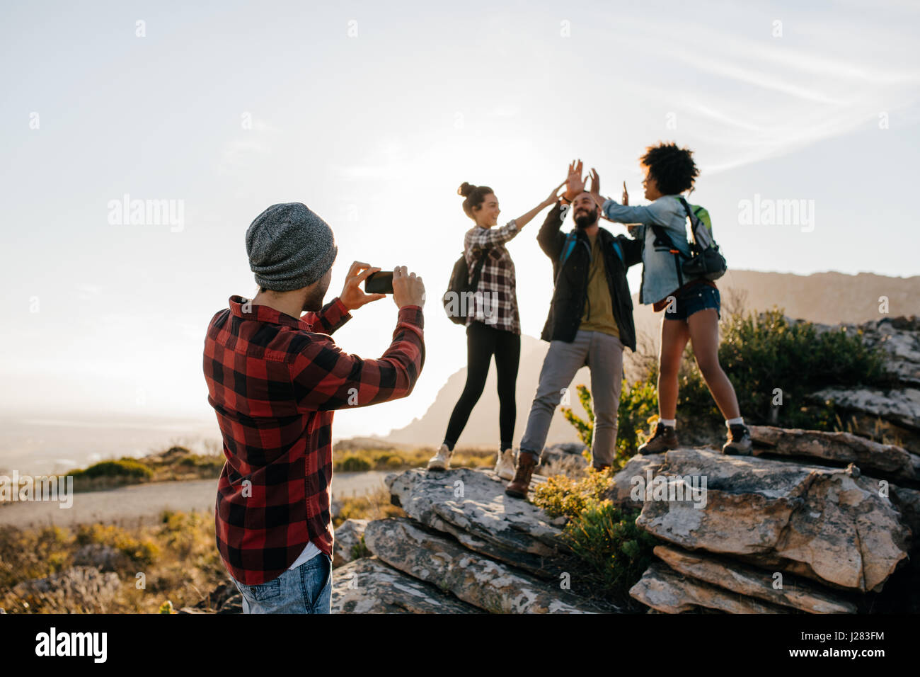 Jeune homme à prendre des photos de ses amis faisant cinq haut en campagne tout en randonnée. Groupe de randonneurs bénéficiant pendant les vacances d'été. Banque D'Images