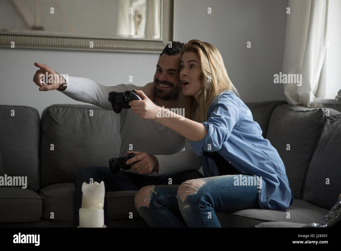 Heureux couple playing video game while sitting on sofa at home Banque D'Images