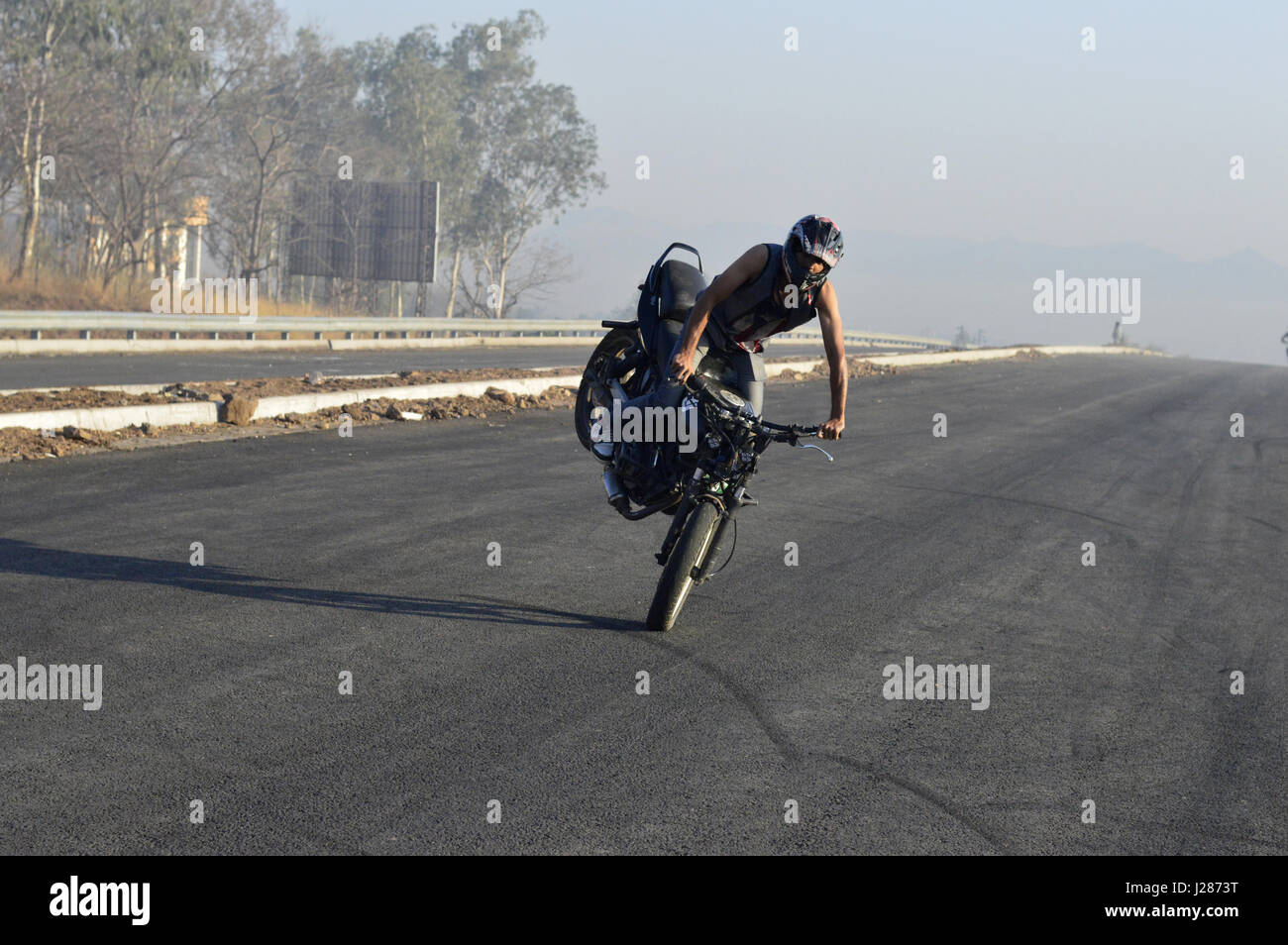 Pilote moto Stunt stoppie faire sur une route locale près de Pune, Maharashtra Banque D'Images