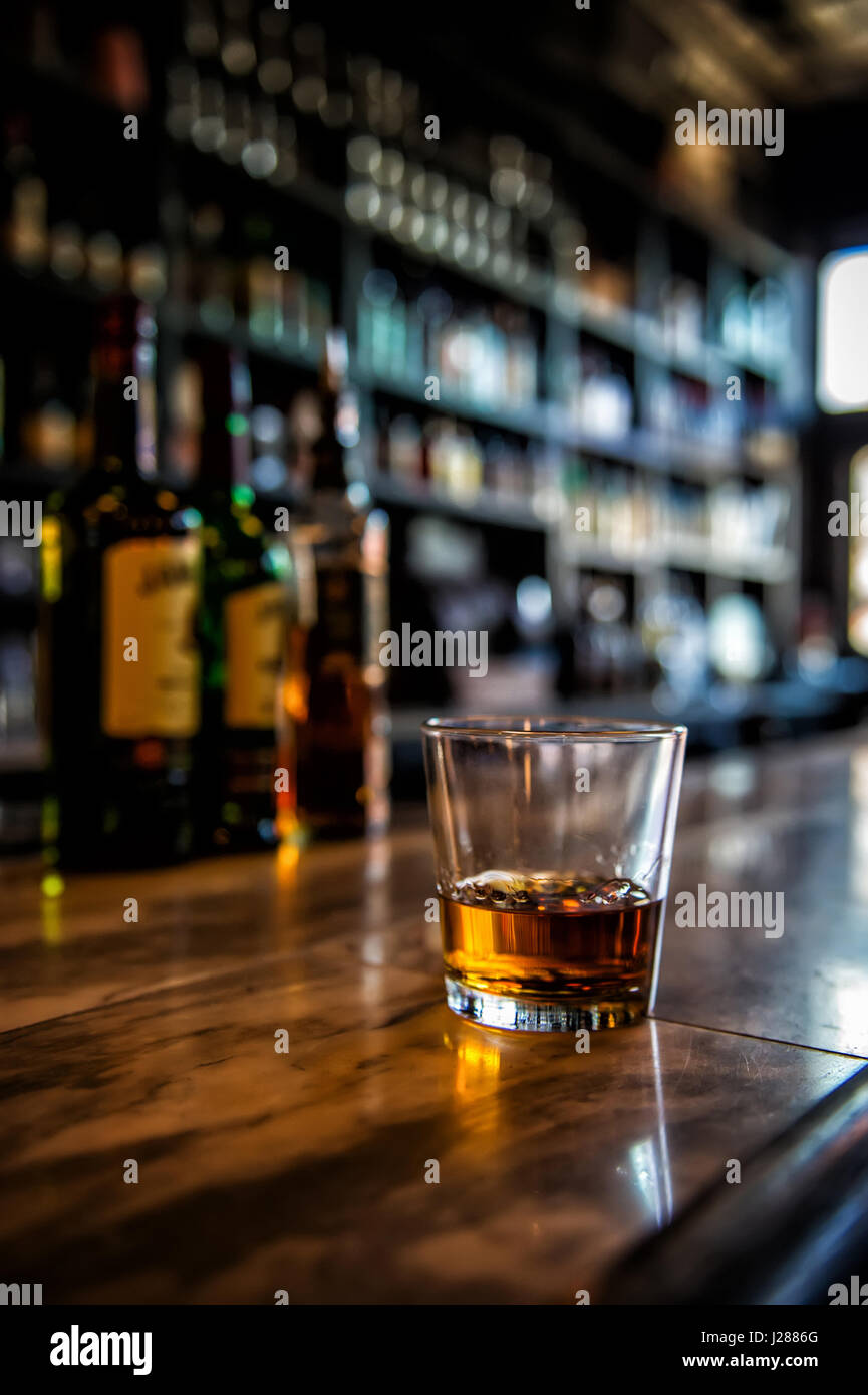 Verre de whisky assis sur un bar avec des bouteilles en arrière-plan Photo  Stock - Alamy