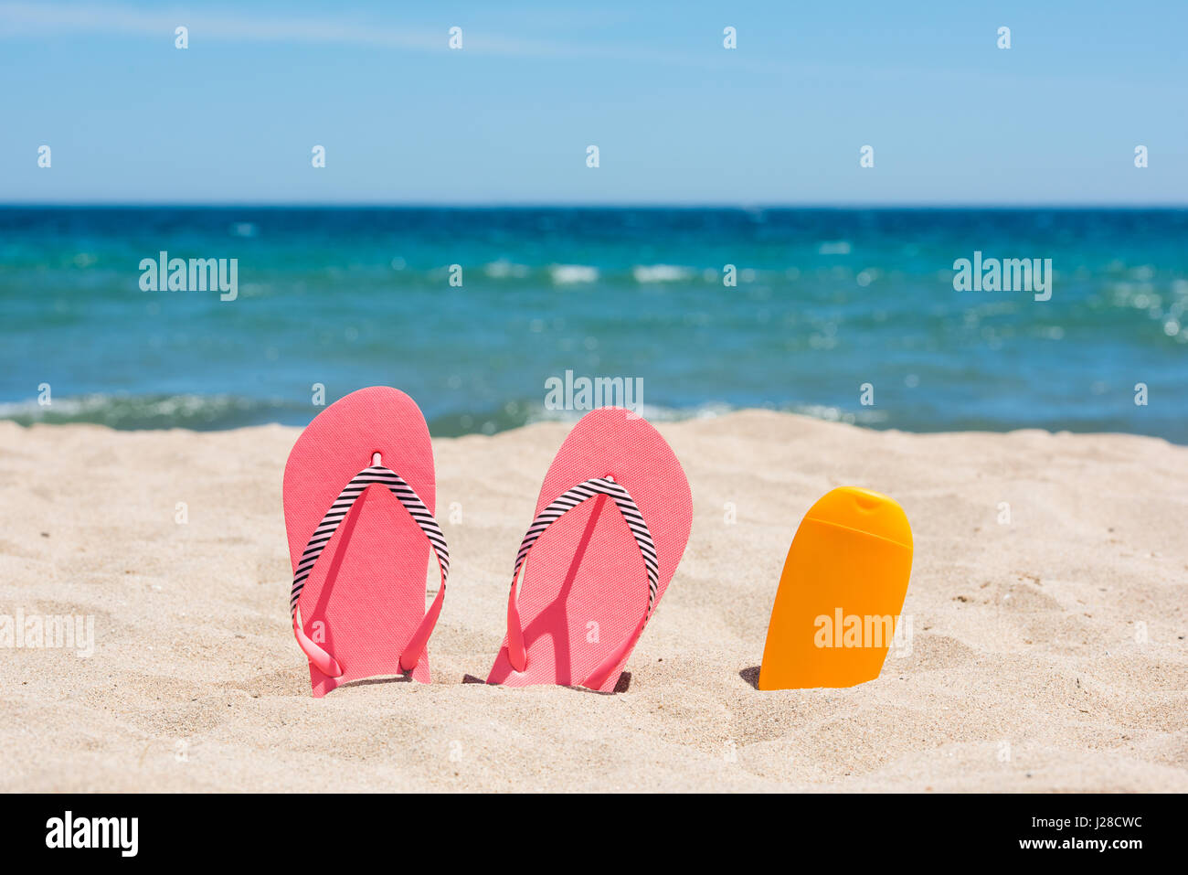 Bouteille d'écran solaire et rose tongs sur la plage Banque D'Images