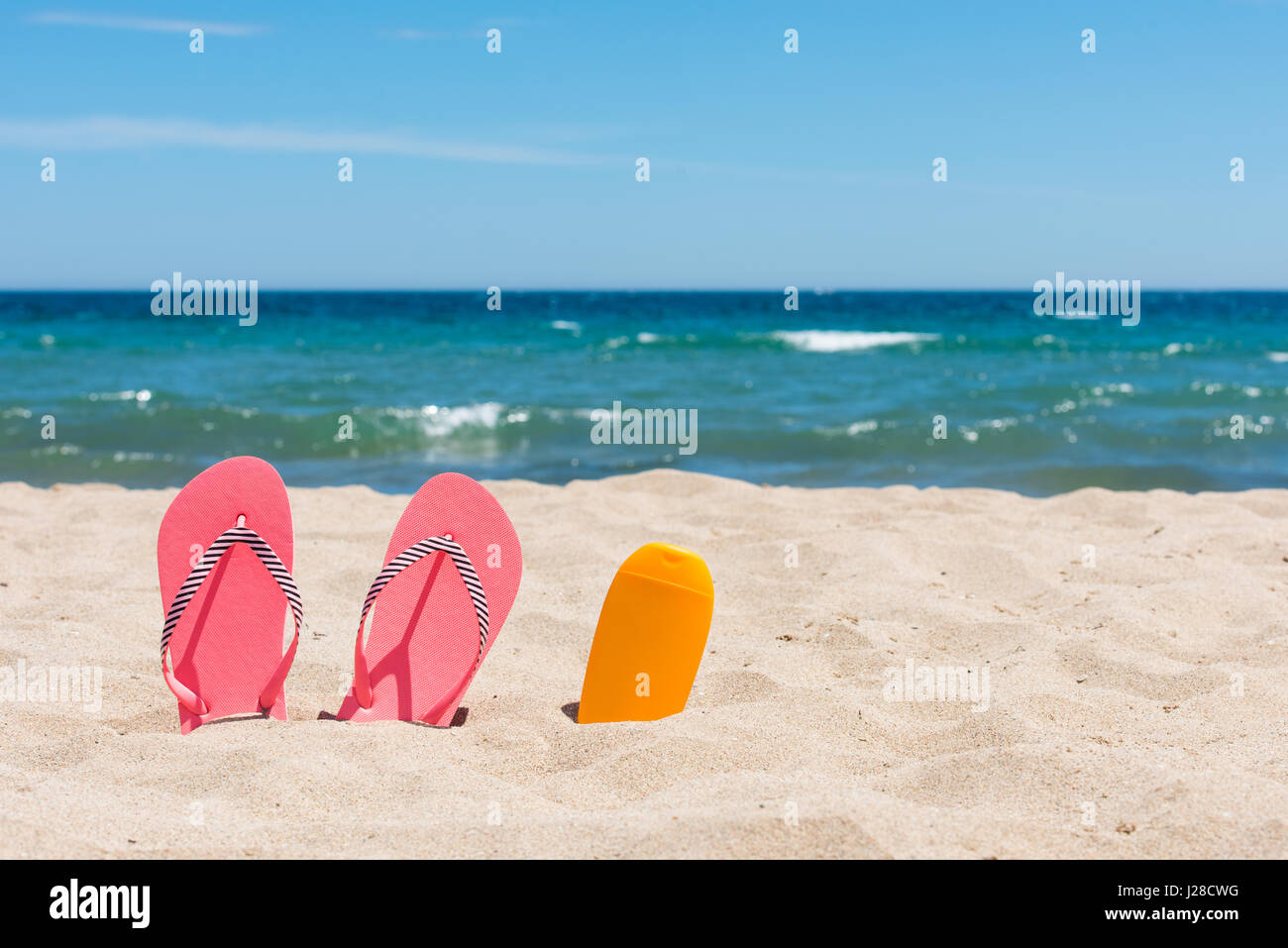 Bouteille d'écran solaire et rose tongs sur la plage Banque D'Images