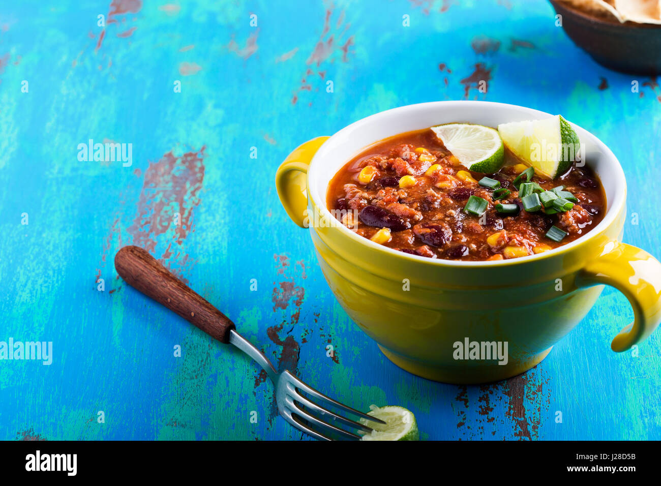 Chili con carne servi en ragoût bol jaune sur bleu table en bois rustique, la cuisine mexicaine Banque D'Images