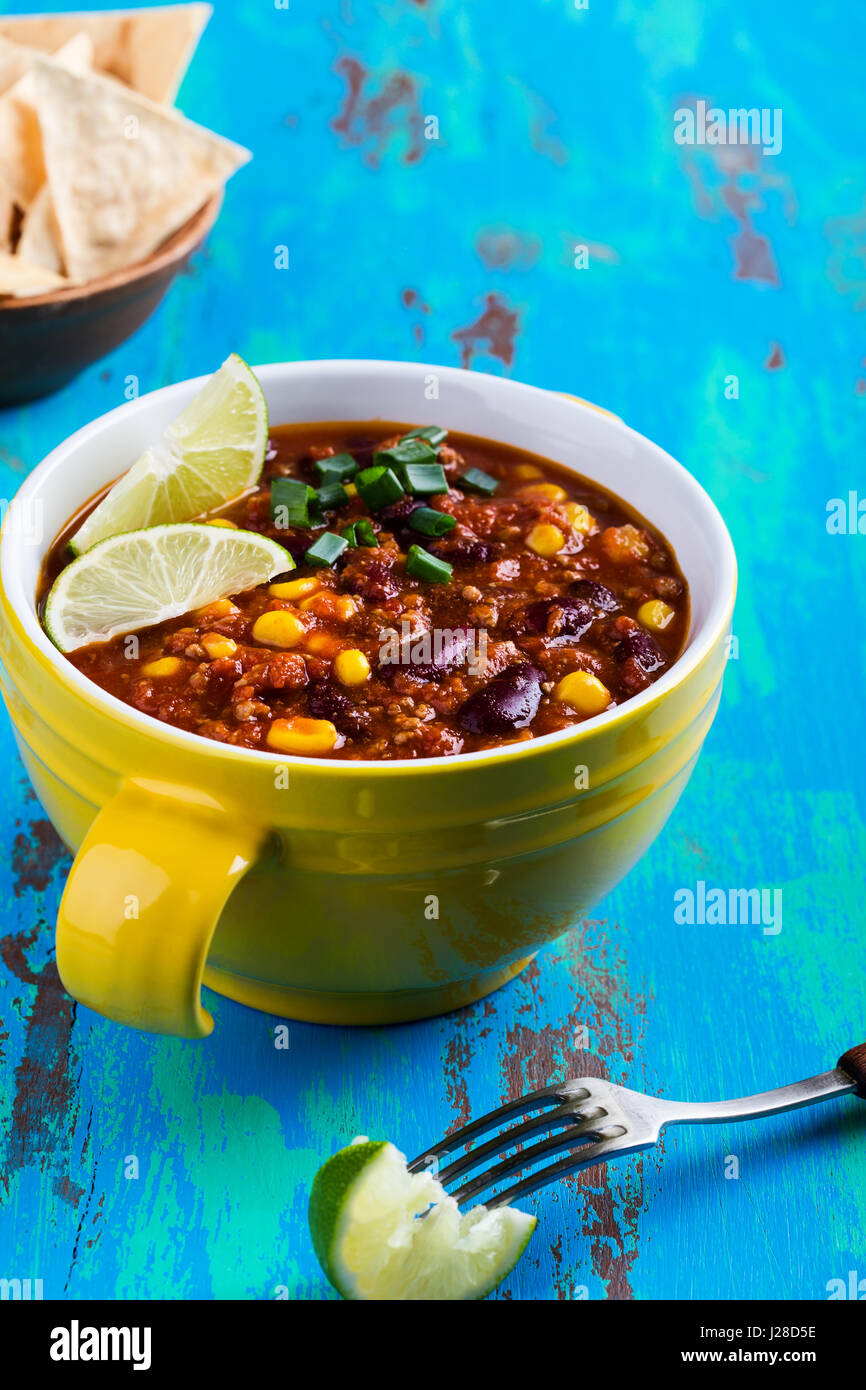 Chili con carne servi en ragoût bol jaune sur bleu table en bois rustique, la cuisine mexicaine Banque D'Images