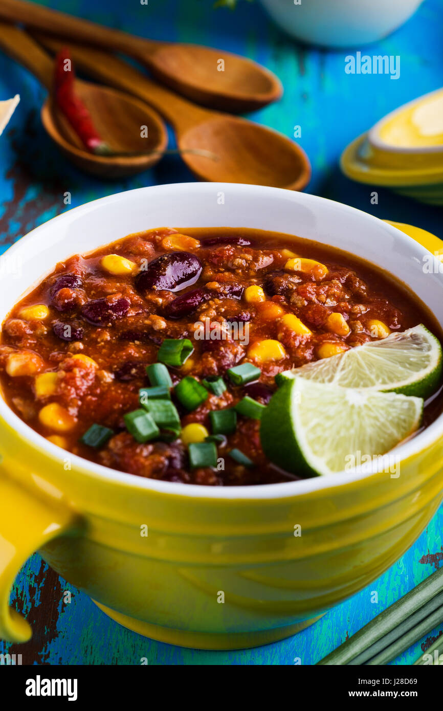 Chili con carne servi en ragoût bol jaune sur bleu table en bois rustique, la cuisine mexicaine Banque D'Images