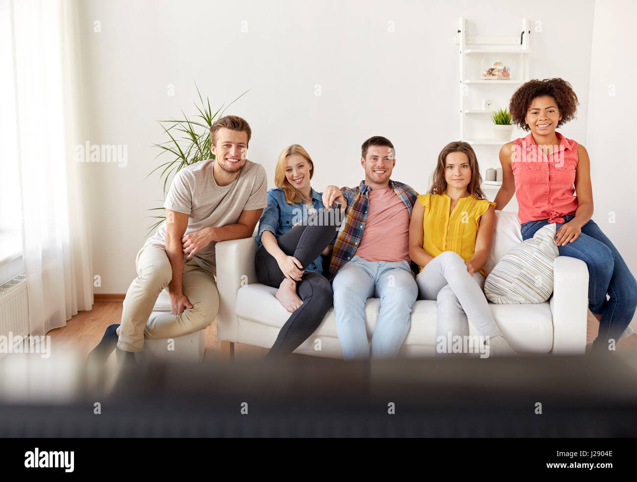 Heureux avec des amis à la maison à regarder la télévision à distance Banque D'Images