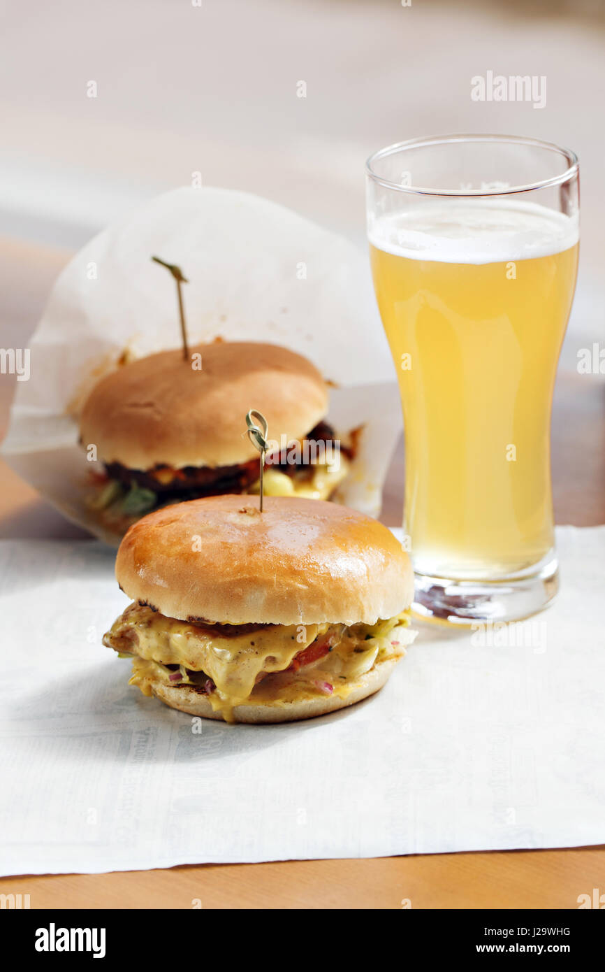 Deux délicieux bien fait burger garni d'oignons, tomates, laitue et tranches de fromage cheddar avec chips nacho sur une planche à découper et le verre de bière en arrière-plan Banque D'Images