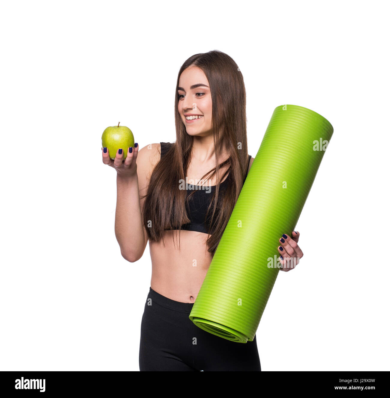Portrait of smiling young woman holding rolled up exercice tapis de yoga et pomme verte isolée sur fond blanc Banque D'Images