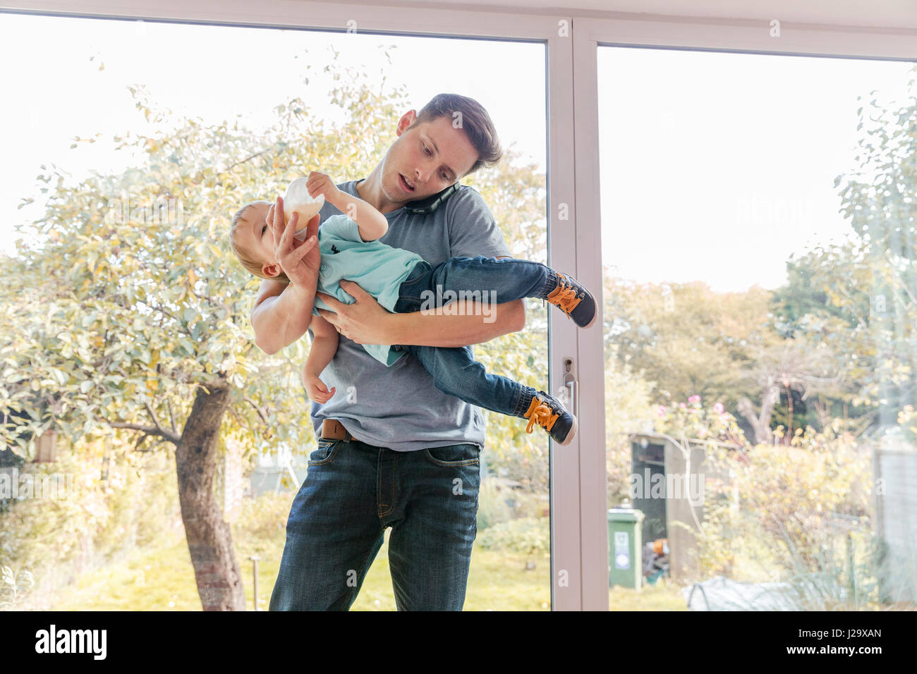 Père holding petit garçon tandis que sur le téléphone à la maison, par fenêtre Banque D'Images