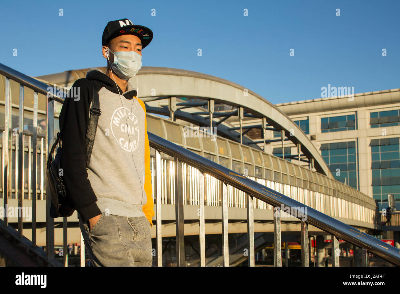 La Chine, Beijing, Morning sun lights young man wearing mask contre la pollution atmosphérique tout en marchant sur un pont près de la Gare Centrale de Pékin le long Second Ring Road dans le district de Dongcheng Banque D'Images