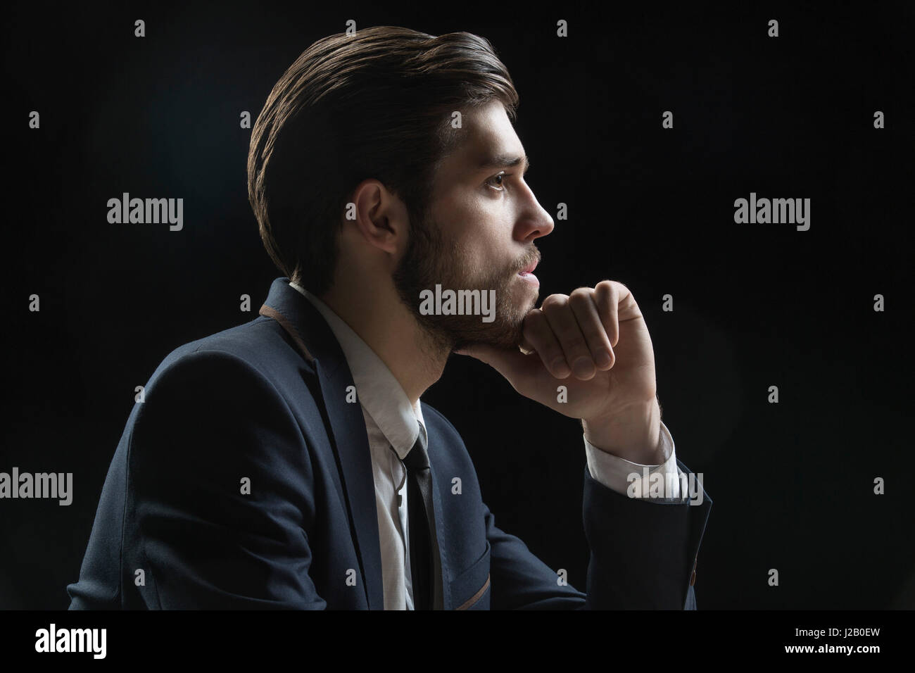 Side view of thoughtful businessman with hand on chin sur fond noir Banque D'Images