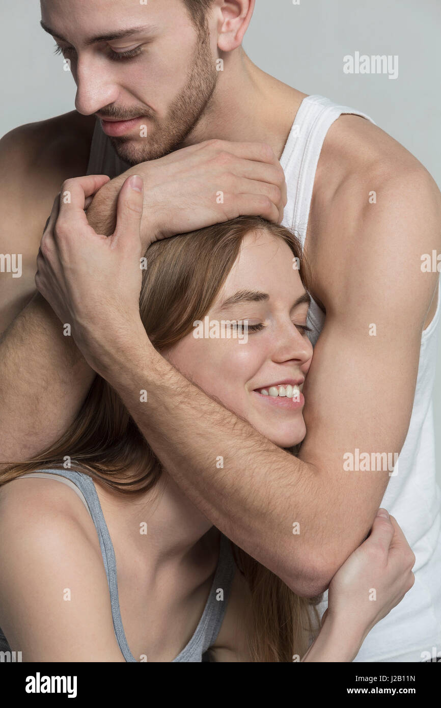 Man embracing smiling girlfriend contre l'arrière-plan gris Banque D'Images