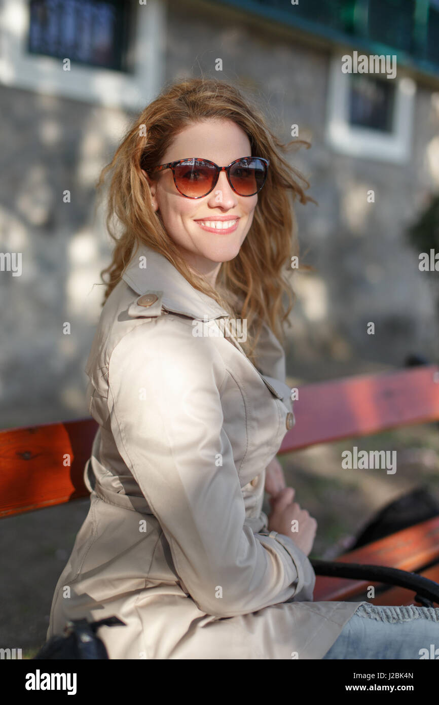 Jeune femme douce en lunettes avec dents sourire assis sur un banc de parc, printemps Banque D'Images