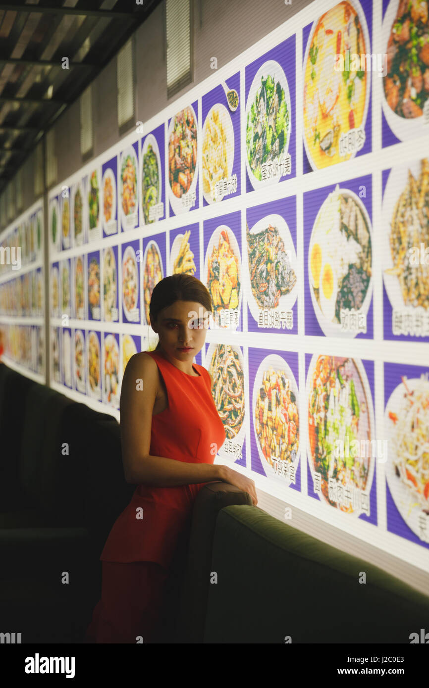 Vue latérale du mystère femme en costume qui, debout près de la mur avec menu et à la voiture. Vertical image Banque D'Images