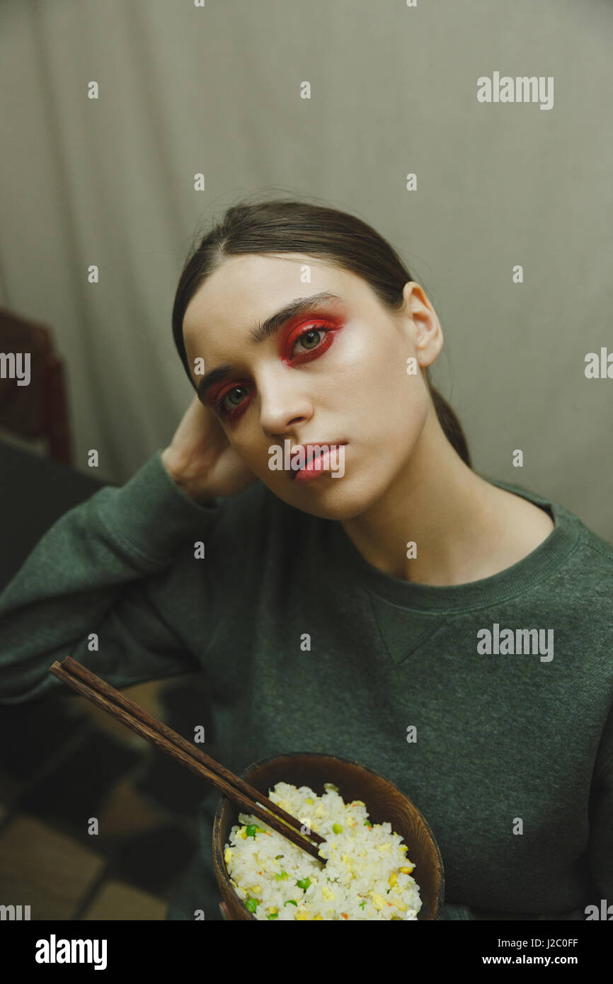 Photo verticale d'un mystère woman in sweater maintenant la plaque de riz tout en étant dans l'Eatery et regardant la caméra Banque D'Images