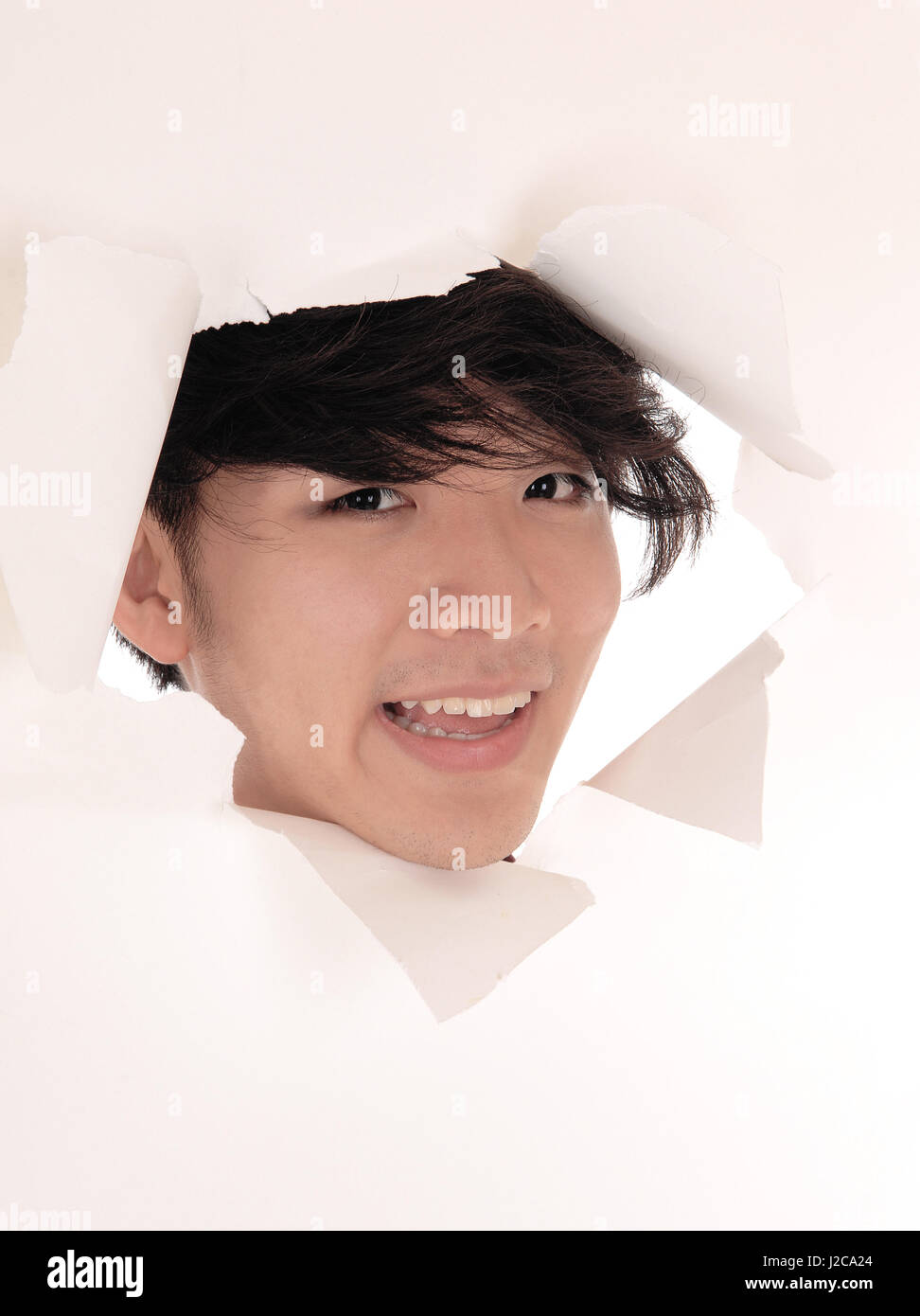 A smiling Asian man à travers un trou dans un papier, souriant, avec des cheveux noirs, isolés pour fond blanc. Banque D'Images