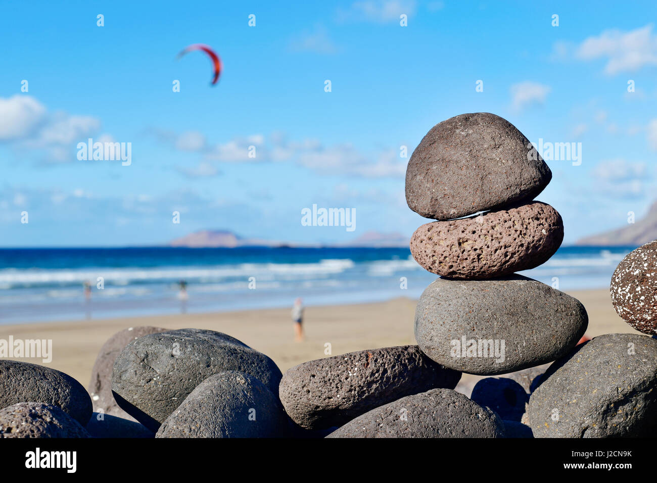 Une vue de la plage de Famara Lanzarote, Canaries, Espagne, avec un tas de pierres au premier plan équilibré et certains kitesurfers et La Graciosa Banque D'Images