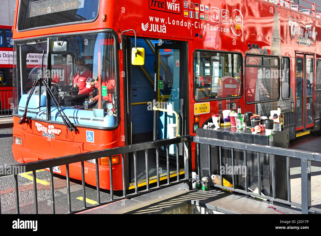 Red tour bus s'arrête à l'arrêt de bus sur le pont de Londres à côté du cabinet de la chaussée utilisée comme dépotoir pour tasses à café boissons en bouteilles et cannettes jonchant Londres Banque D'Images
