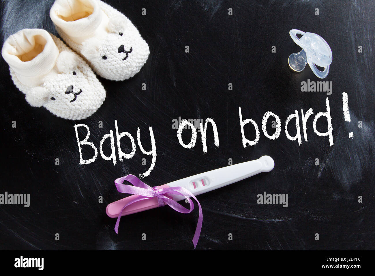 'Bébé à bord' inscription sur tableau noir avec test de grossesse positif et chaussures de bébé Banque D'Images
