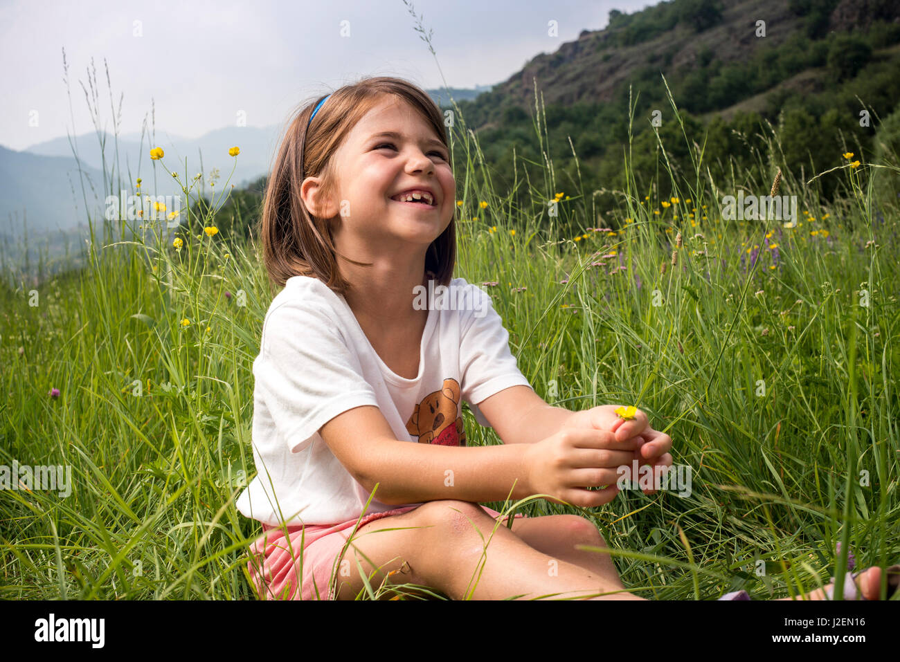 Souriante jeune fille assise dans le champ de fleurs sauvages Banque D'Images