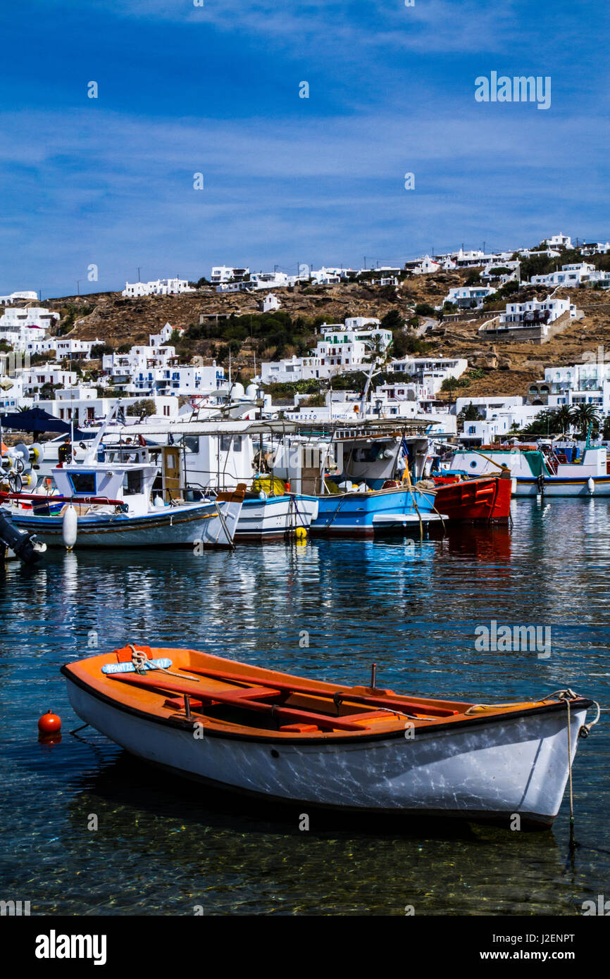 Mykonos, Grèce. Orange et blanc voile flotte dans l'eau avec les autres bateaux colorés avec les bâtiments blancs sur la colline Banque D'Images