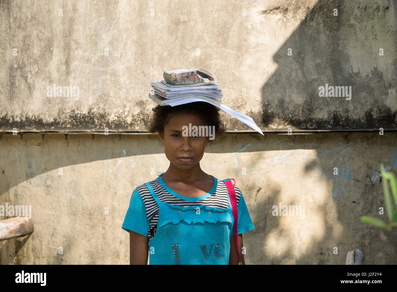 En Mélanésie, la Papouasie-Nouvelle-Guinée, l'île de dobu. école de village. Jeune écolière avec lesson books sur sa tête. Banque D'Images