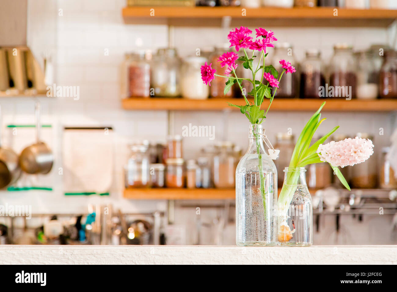 Fleurs dans deux vases dans une cuisine blanche avec étagères en bois pourvue d'épices. Violet, fuchsia, rose et fleurs. Banque D'Images