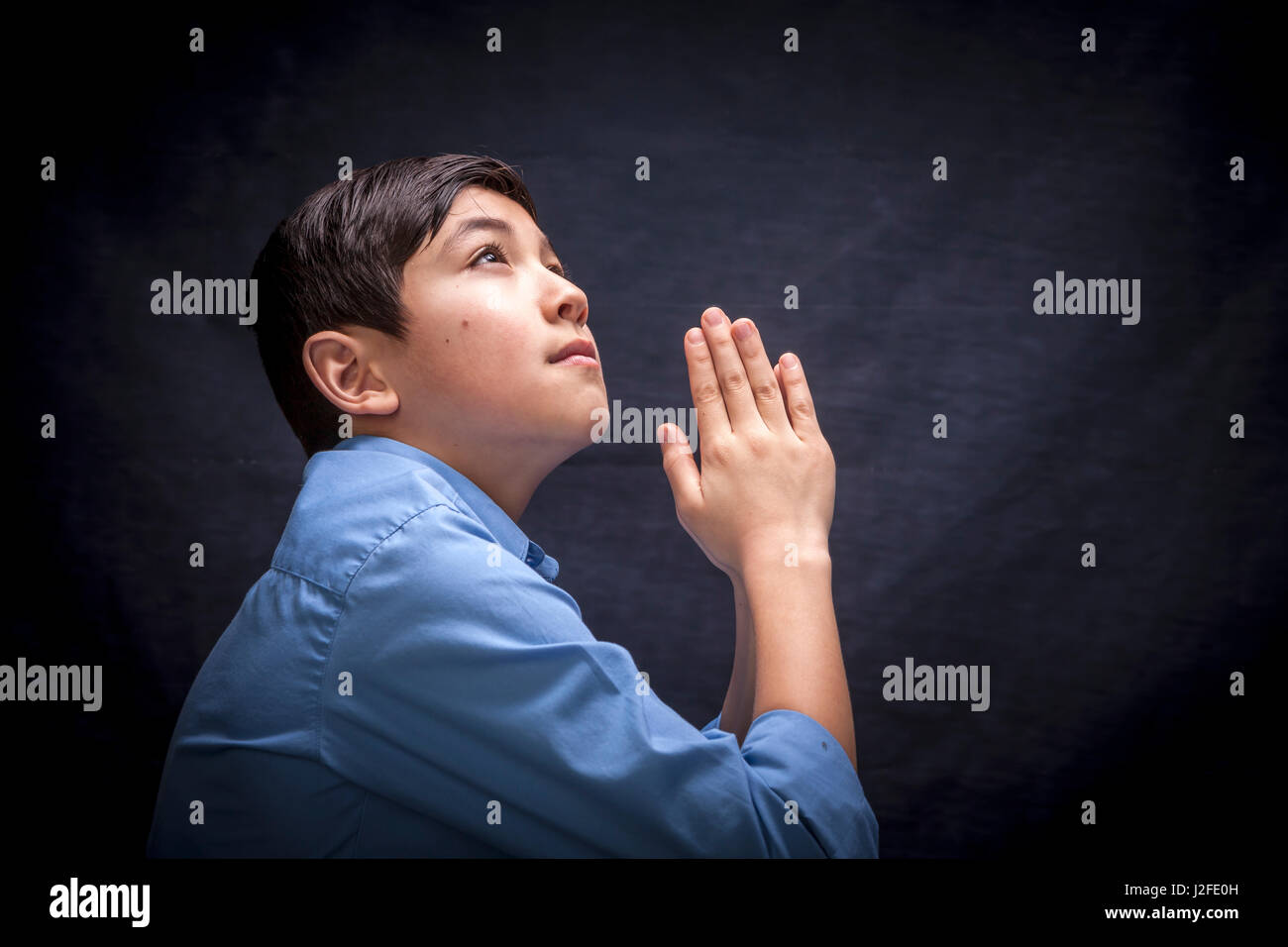 Un jeune garçon se replie ses mains et soulève sa tête dans la prière à Dieu. Banque D'Images