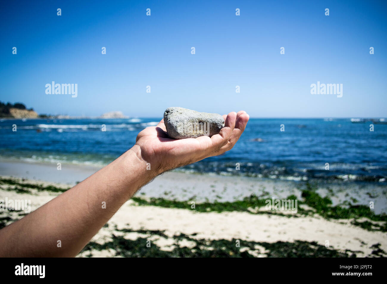 Main jetant une pierre en l'air avec la plage en arrière-plan Banque D'Images