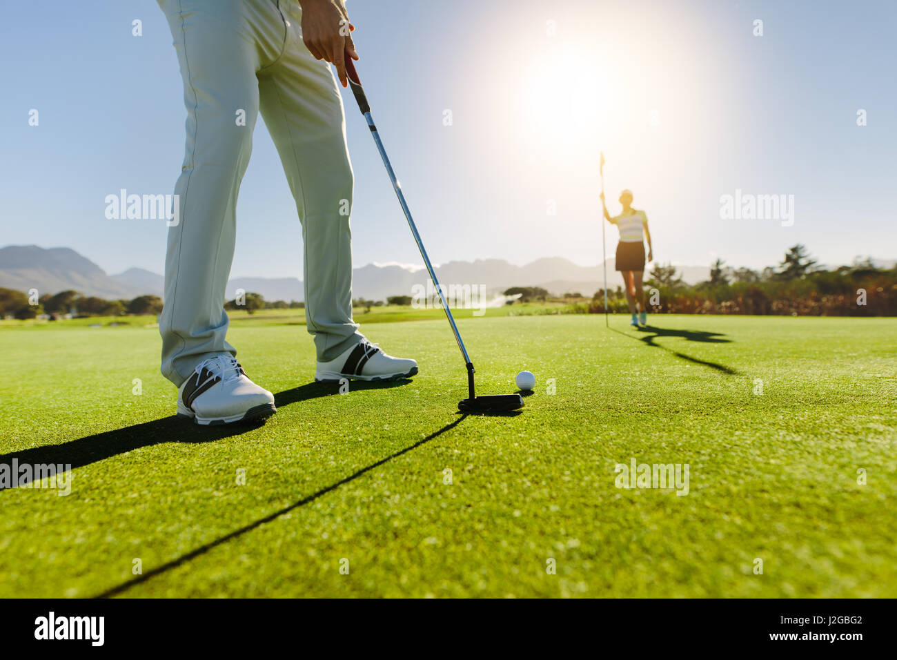 Low angle view of golfeur sur putting green sur le point de prendre la photo. Homme joueur de golf putting on vert avec deuxième joueuse dans l'arrière-plan vertige Banque D'Images