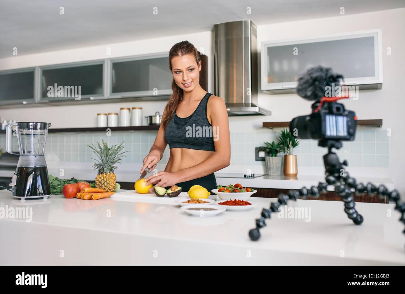 Jeune femme l'enregistrement des aliments en fonction du contenu vidéo sur appareil photo. Smiling woman cutting fruits et légumes dans la cuisine. Banque D'Images