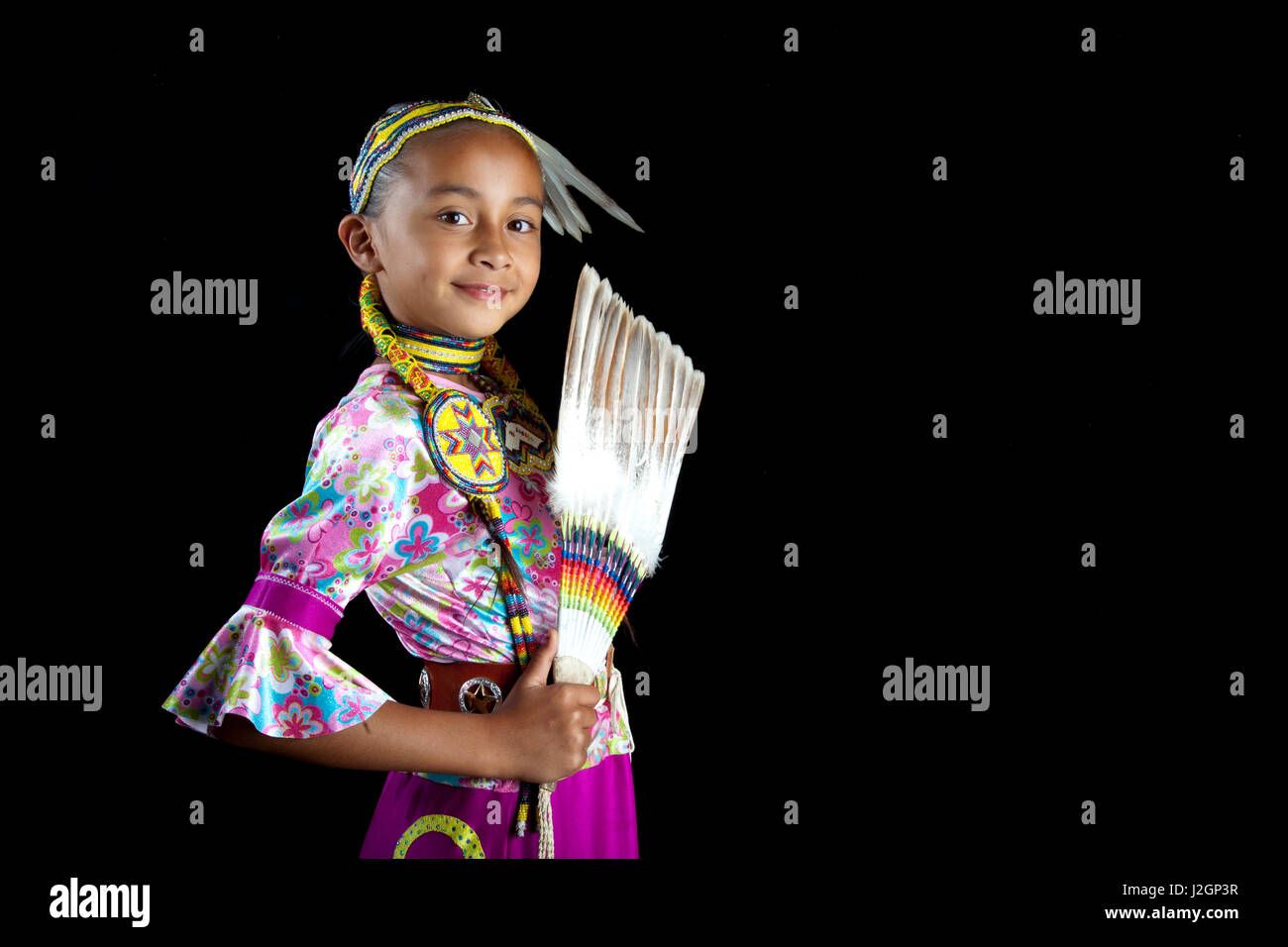 Danseuse traditionnelle de pow-wow 9 ans Jaydean (Lakota) vêtus de costumes colorés et bande de cheveux perlés contient jusqu'a feather fan d'un fond noir. Banque D'Images