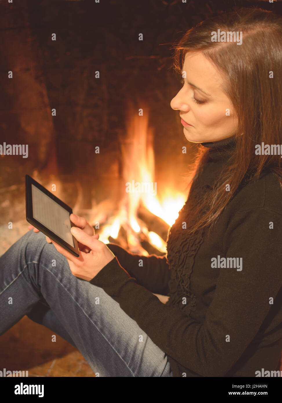 Jolie femme ebook lecture assis près de l'âtre Banque D'Images