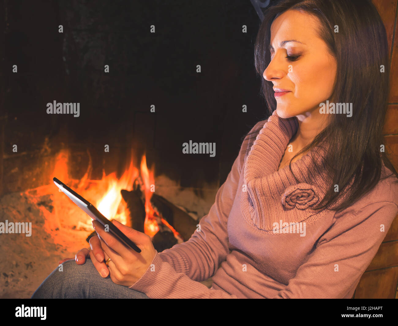 Jolie femme ebook lecture assis près de l'âtre Banque D'Images