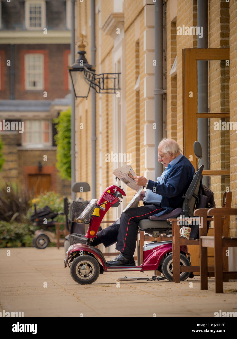 Pensionné Chelsea au Royal Hospital Chelsea, s'est assis sur un scooter de mobilité en dehors de vacances lecture journal, Londres, Royaume-Uni. Banque D'Images