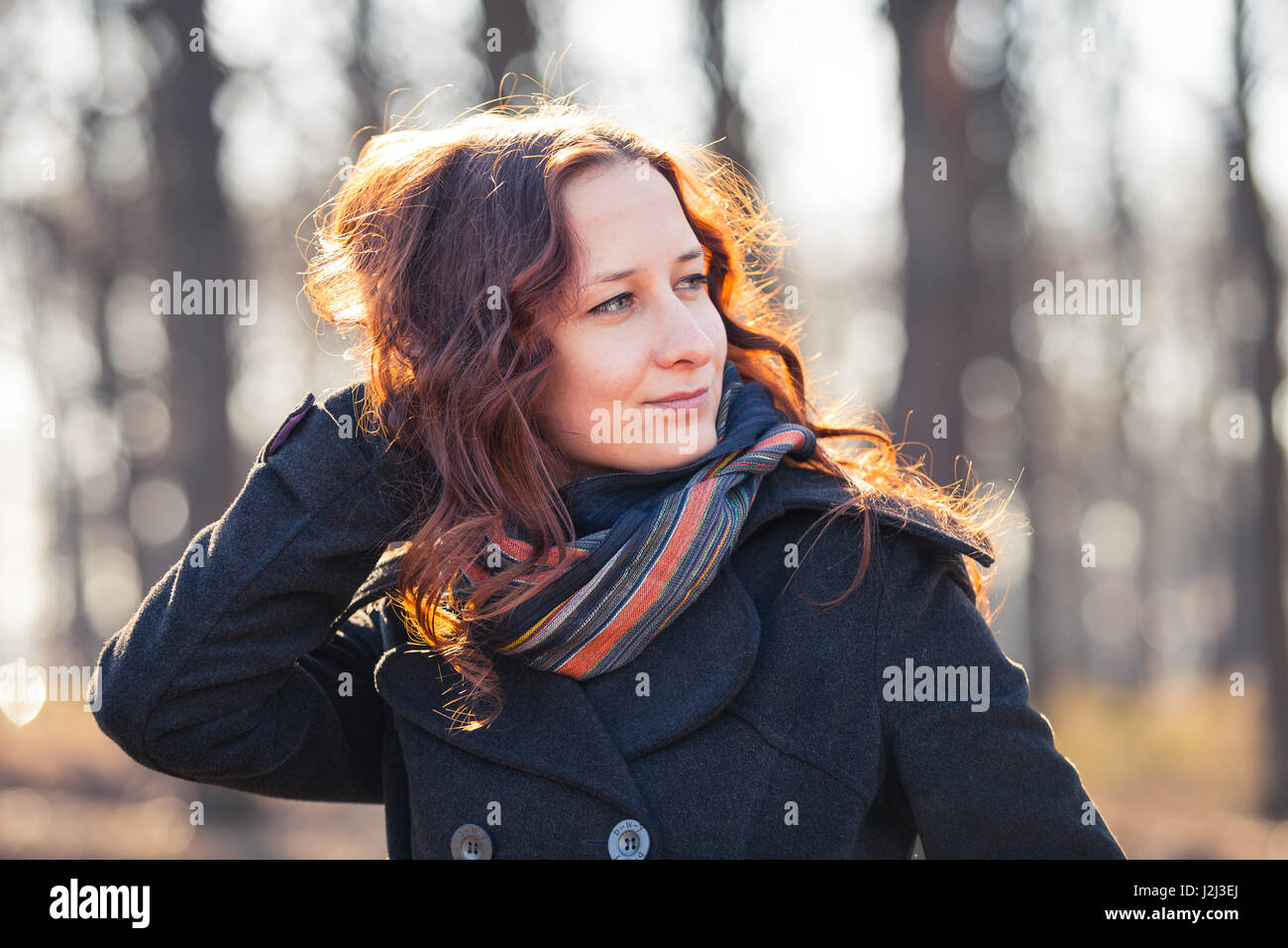 Red-haired girl Smiling outdoors, portée manteau et écharpe. Au début du printemps au park ar le coucher du soleil. Banque D'Images