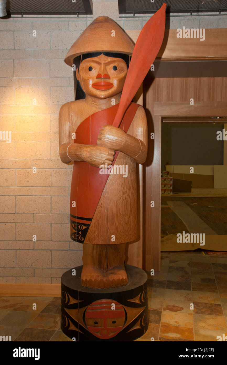 Grand bois de cèdre la sculpture des totems d'un rassemblement des Salish de la côte de l'homme portant un chapeau conique et est titulaire d'une palette à l'affichage à l'Hilbub Centre Culturel et Musée situé sur les Tribus Tulalip Reservation à Marysville, WA Banque D'Images